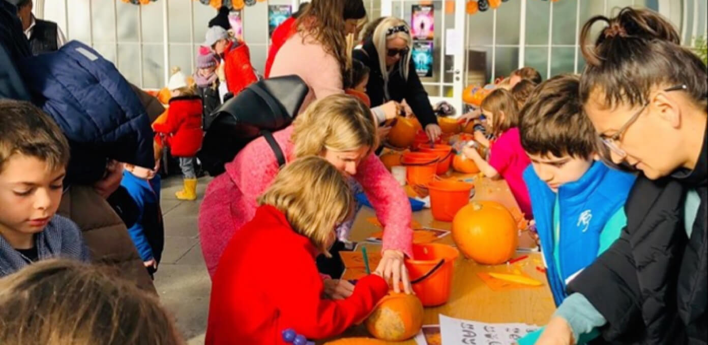 Children with guardians at a table, designing and carving pumpkins