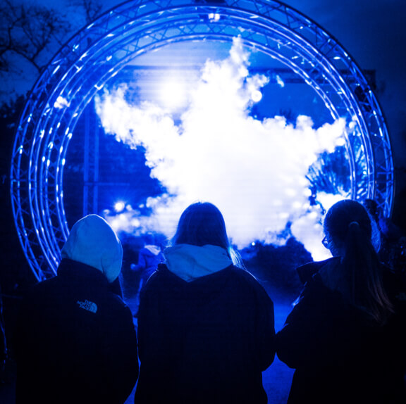 Three people looking into a tunnel of smoke illuminated by blue lights