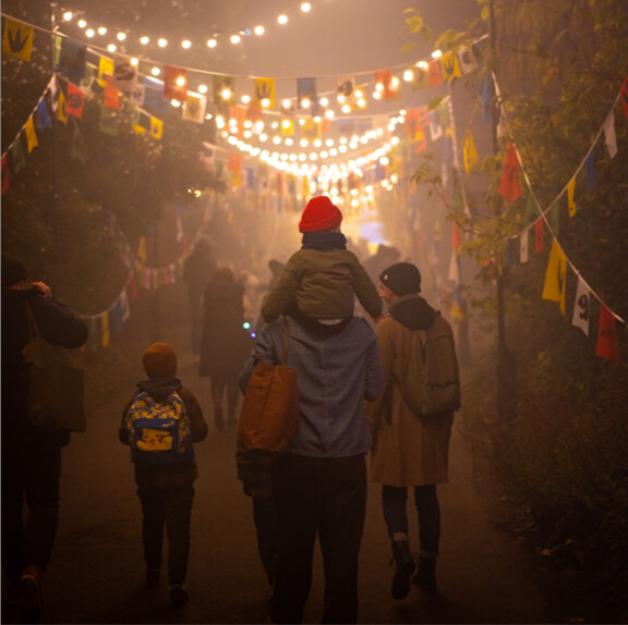 Silhouettes of a family walking through a pathway decorated with colourful bunting and illuminated by strings of light