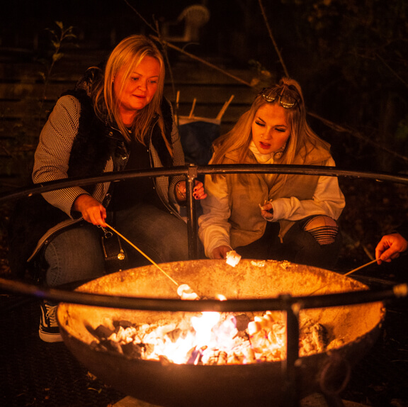 An adult and teenager toasting marshmallows over an oepn fire pit