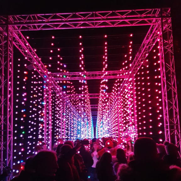 Silhouettes of a large group of people walking through a tunnel of hanging illuminated strings of pink lights